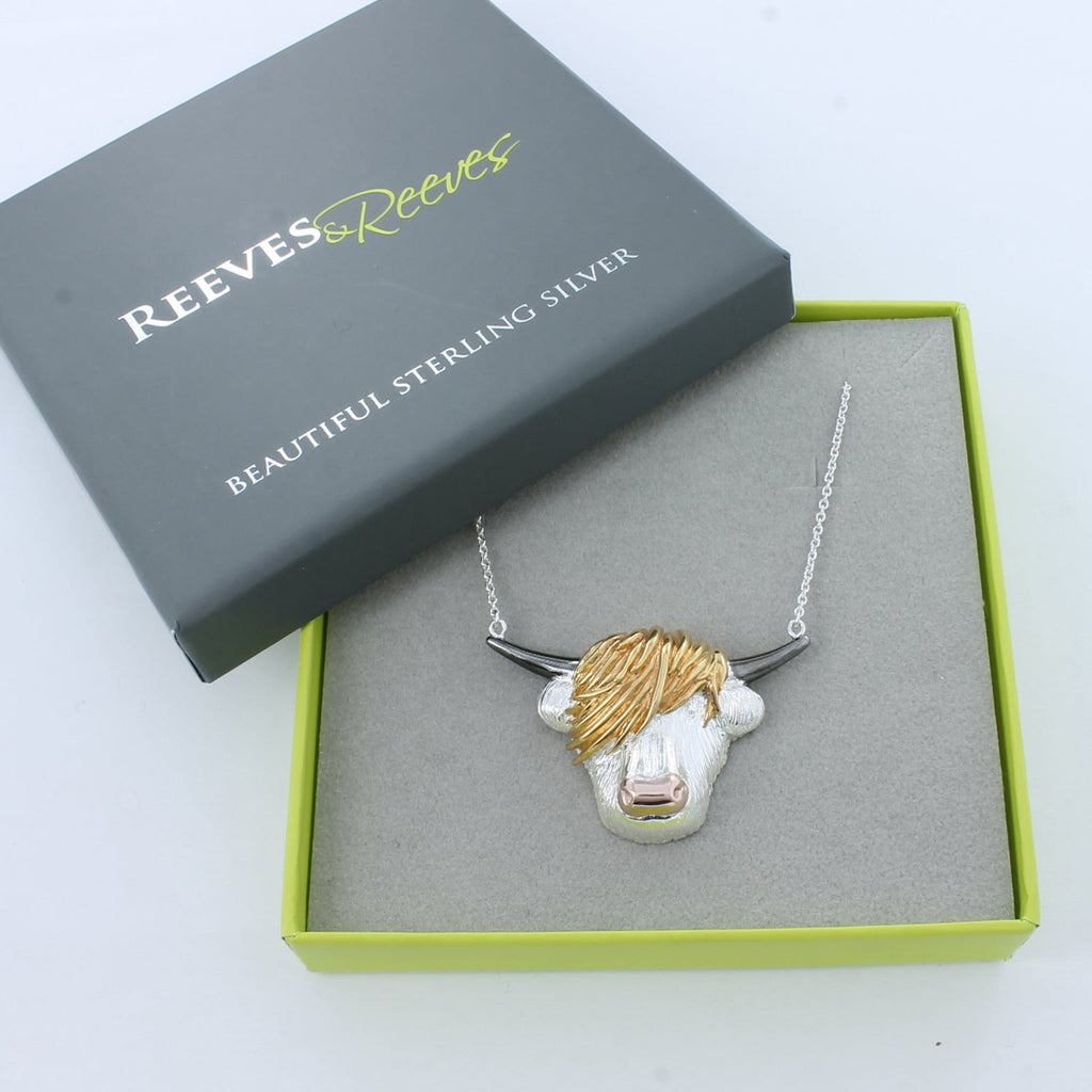 A supersize Highland Cow face, with 18ct rose gold nose, 18ct yellow gold hair and black ruthenium horns, sat centrally on a fine silver chain and shown in a Reeves & Reeves grey and green gift box.