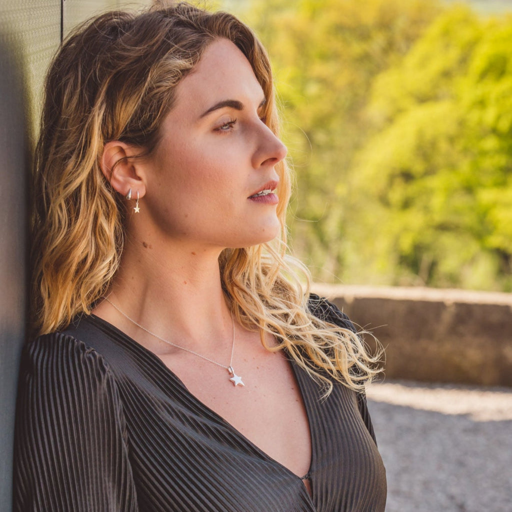 A silver solid star necklace, hung on a silver chain and worn on a model.