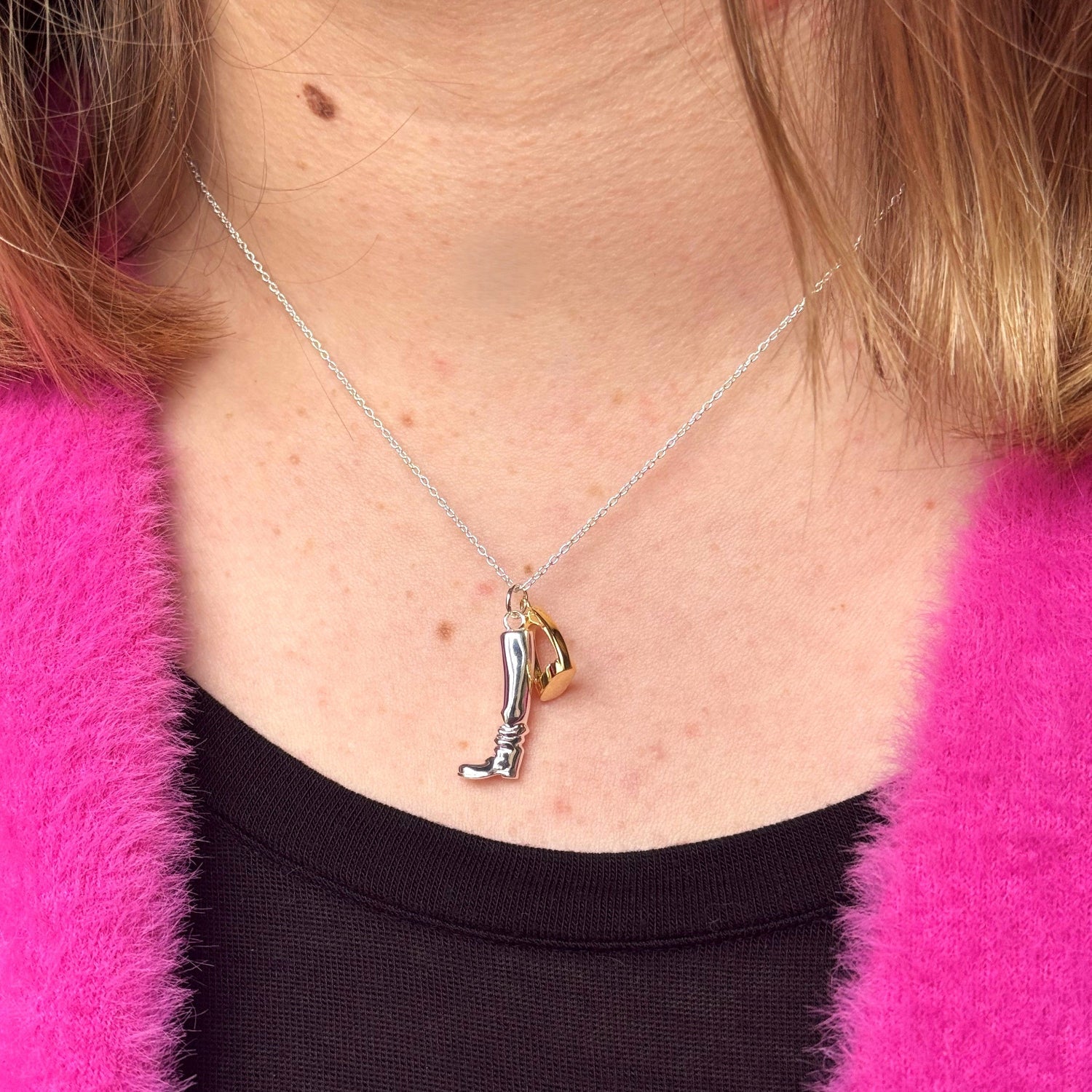 A sterling silver riding boot charm, hung next to an 18ct gold plated stirrup and both hung on a silver adjustable chain and worn on a models neck.
