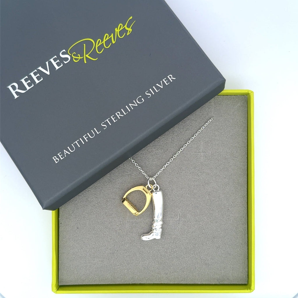 A sterling silver riding boot charm, hung next to an 18ct gold plated stirrup charm, both hung next to each other on a silver chain and shown in a Reeves & Reeves gift box.