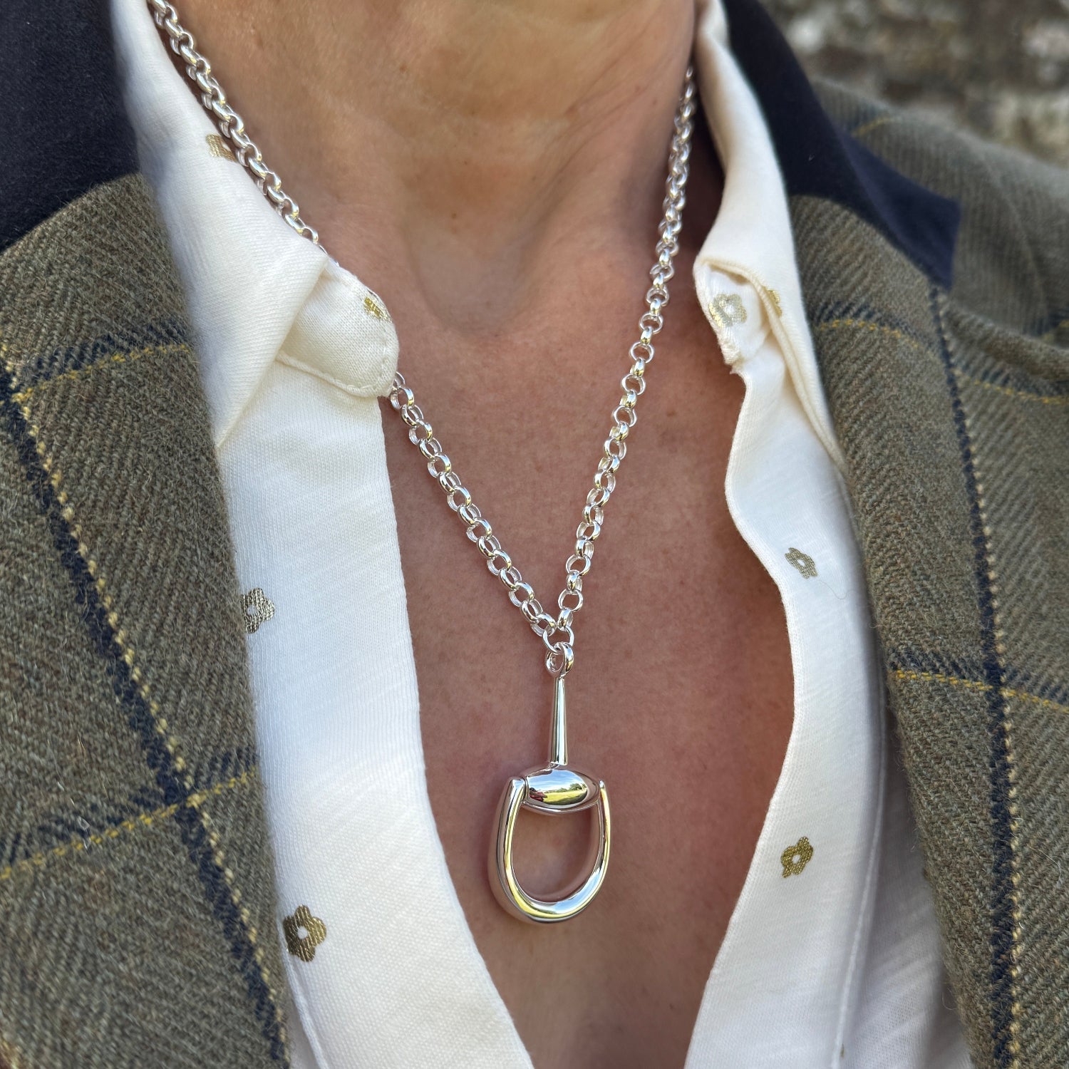 A sterling silver necklace, with a half snaffle in supersize shown as the central feature and hanging on a thick oval link chain. Worn on a model.