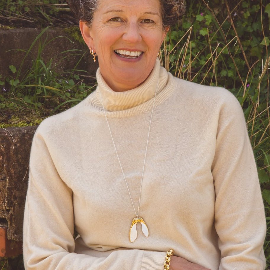 A sterling silver supersize sycamore with 18ct gold plated detail, worn on a long chain on a lady over the top of a jumper.