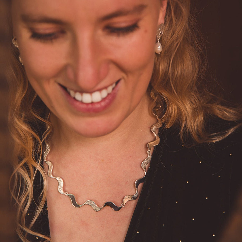 A sterling silver wave necklace with high shine or hammered finish, worn on a ladies neck.