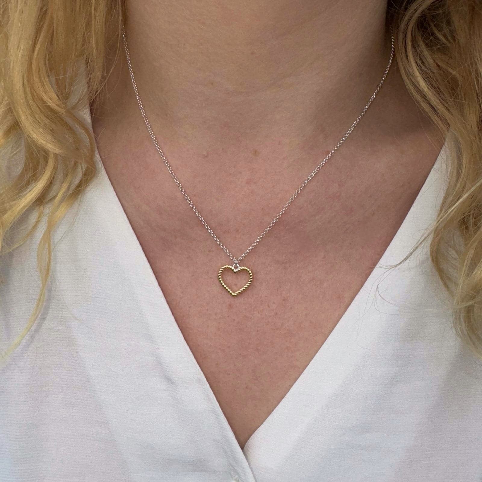 Heart silhouette pendant in sterling silver with gold plating and a twisted design. Hanging on a silver adjustable chain and worn on a model.