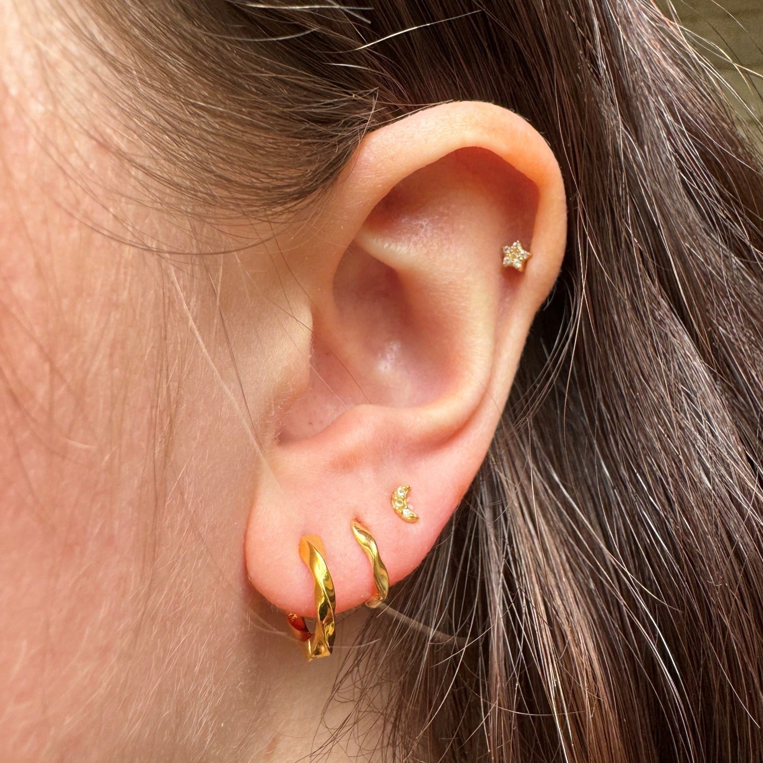 A sterling silver huggie style hoop earring in silver and gold plating, shown in a ladies ear with other piercings.