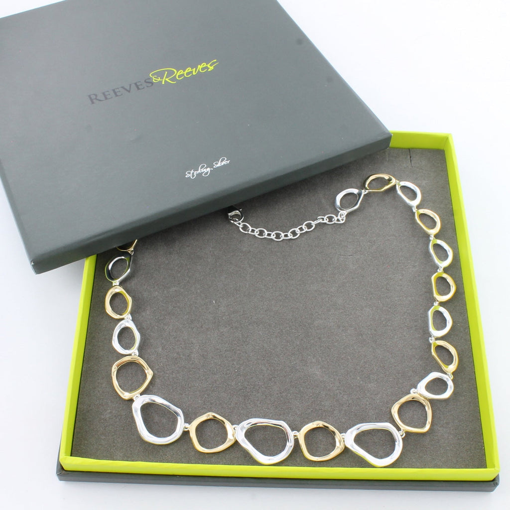 A sterling silver necklace comprised of circles with undulated edges, interspersed with 18ct gold plated rings and shown in a Reeves & Reeves grey and green branded gift box.