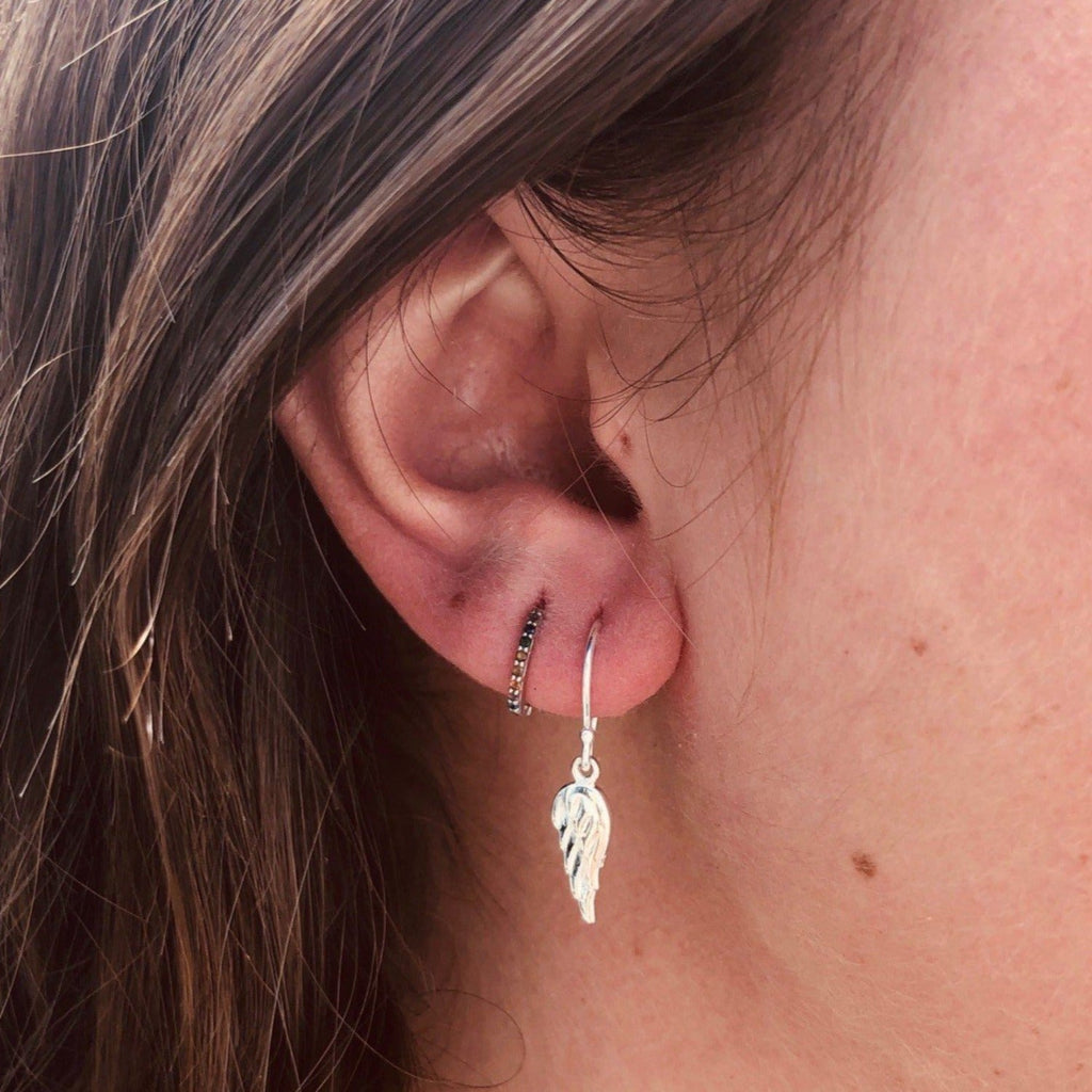 A sterling silver angel wing drop earring, hanging on a silver hook and shown in a ladies ear.