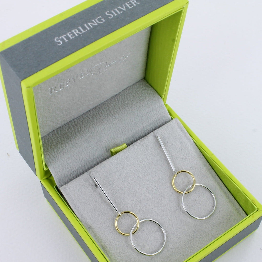 A pair of sterling silver drop earrings, with two interlinking circles hanging from the bottom of a silver bar. One sterling silver and one with 18ct gold plating and shown in a Reeves & Reeves gift box.