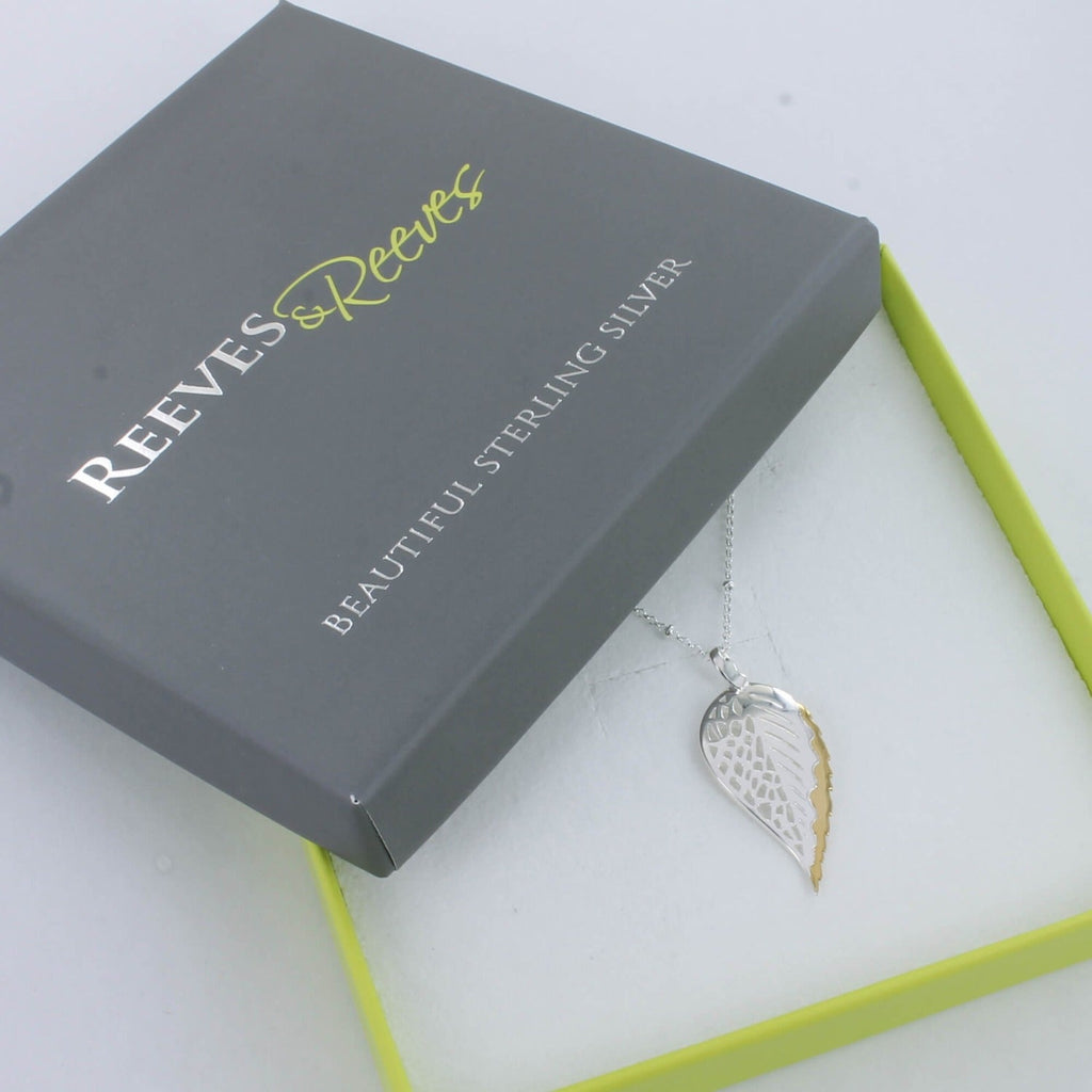 A sterling silver beech leaf necklace with a gold plated edge, hung on a silver chain and shown in a Reeves & Reeves branded gift box.