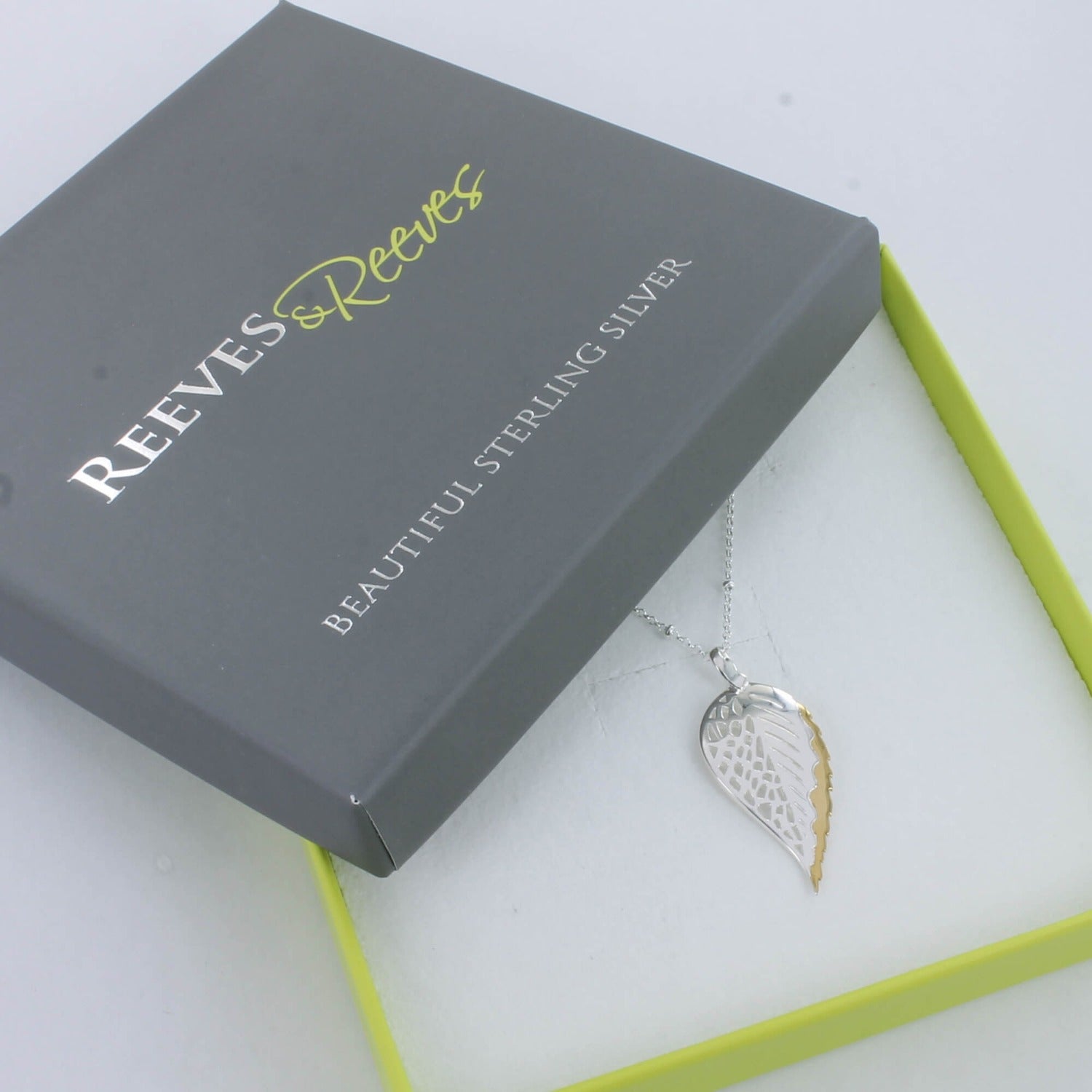 A sterling silver beech leaf necklace with a gold plated edge, hung on a silver chain and shown in a Reeves & Reeves branded gift box.