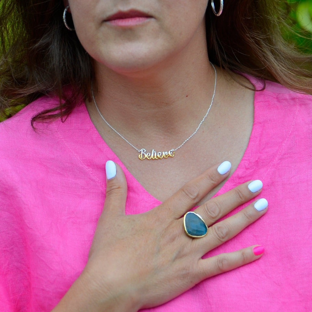 A sterling silver 'believe' necklace hanging centrally on a silver chain. The word 'believe' is half sterling silver and half 18ct gold plate. Worn on a model.
