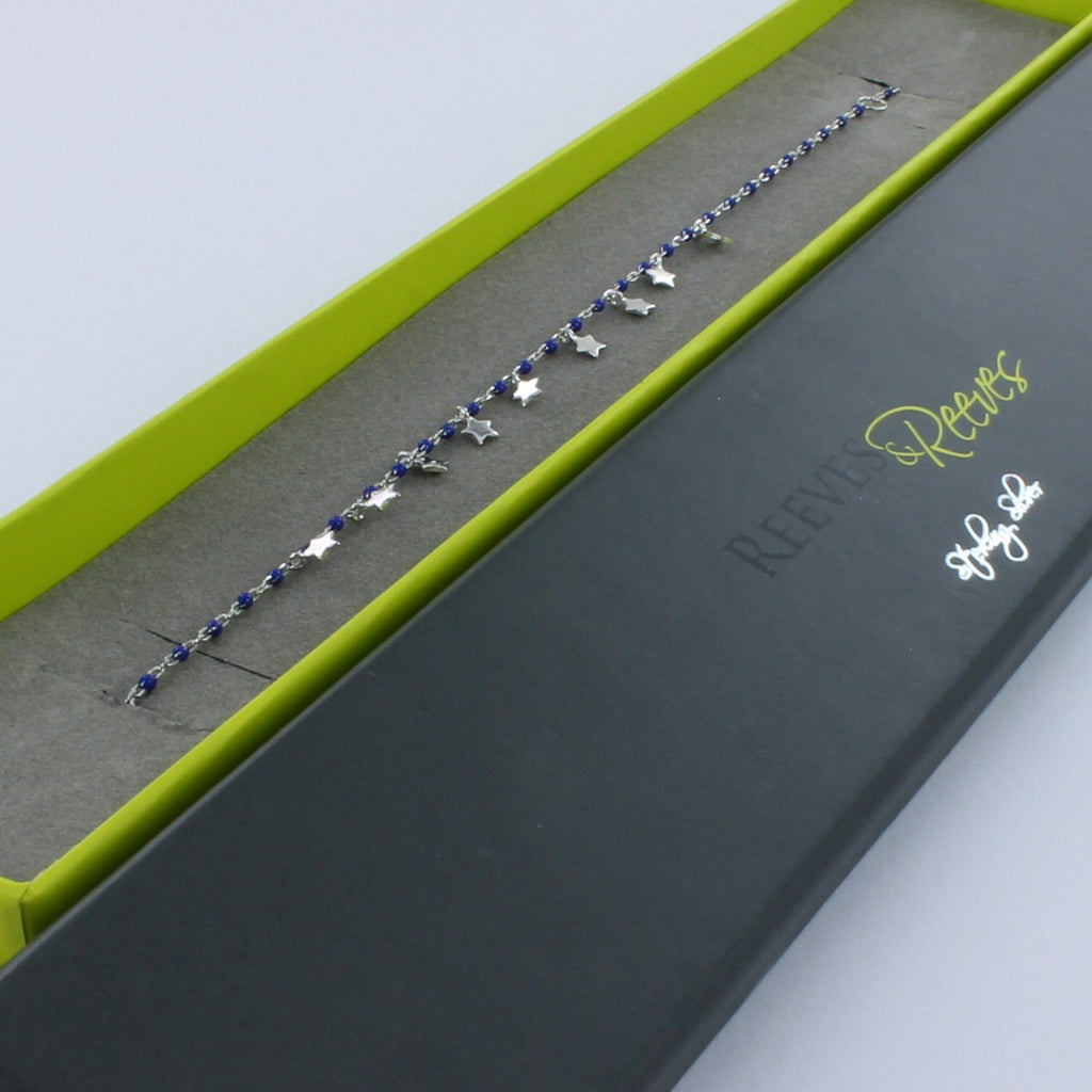 Silver fine chain bracelet with navy blue beads spread evenly along the chain. High shine silver star charms hang from the central part of the chain. Shown in a Reeves & Reeves branded gift box.