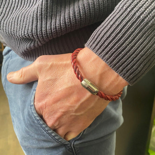 A twisted red leather bracelet, finished with a stainless steel clasp, shown on a mans wrist.