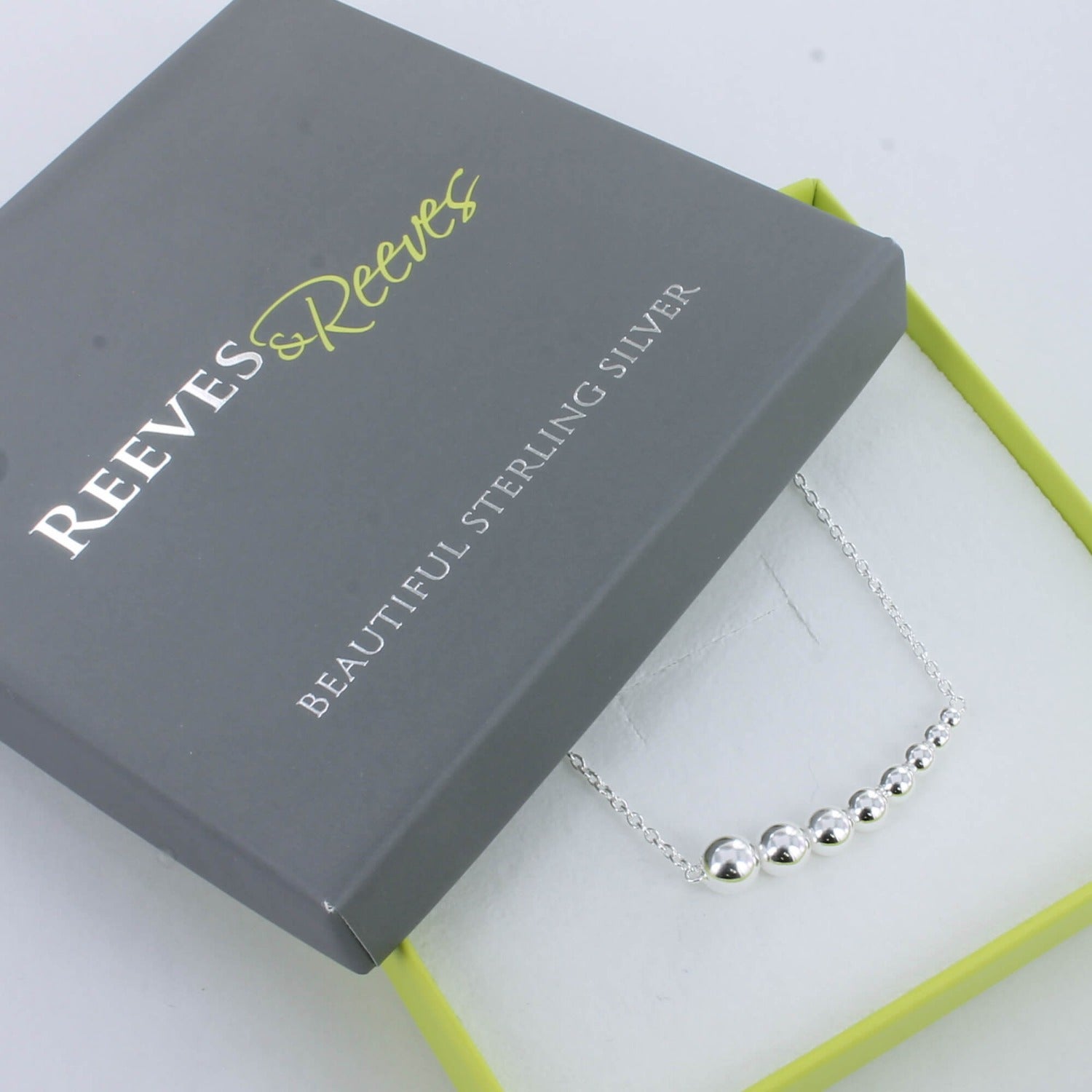 A sterling silver necklace with high shine silver beads that decrease in size from left to right and shown in a Reeves & Reeves gift box.