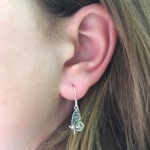 A sterling silver Butterfly Drop Earring, with cut outs in its wings and hanging on a silver hook. Shown in a ladies ear.