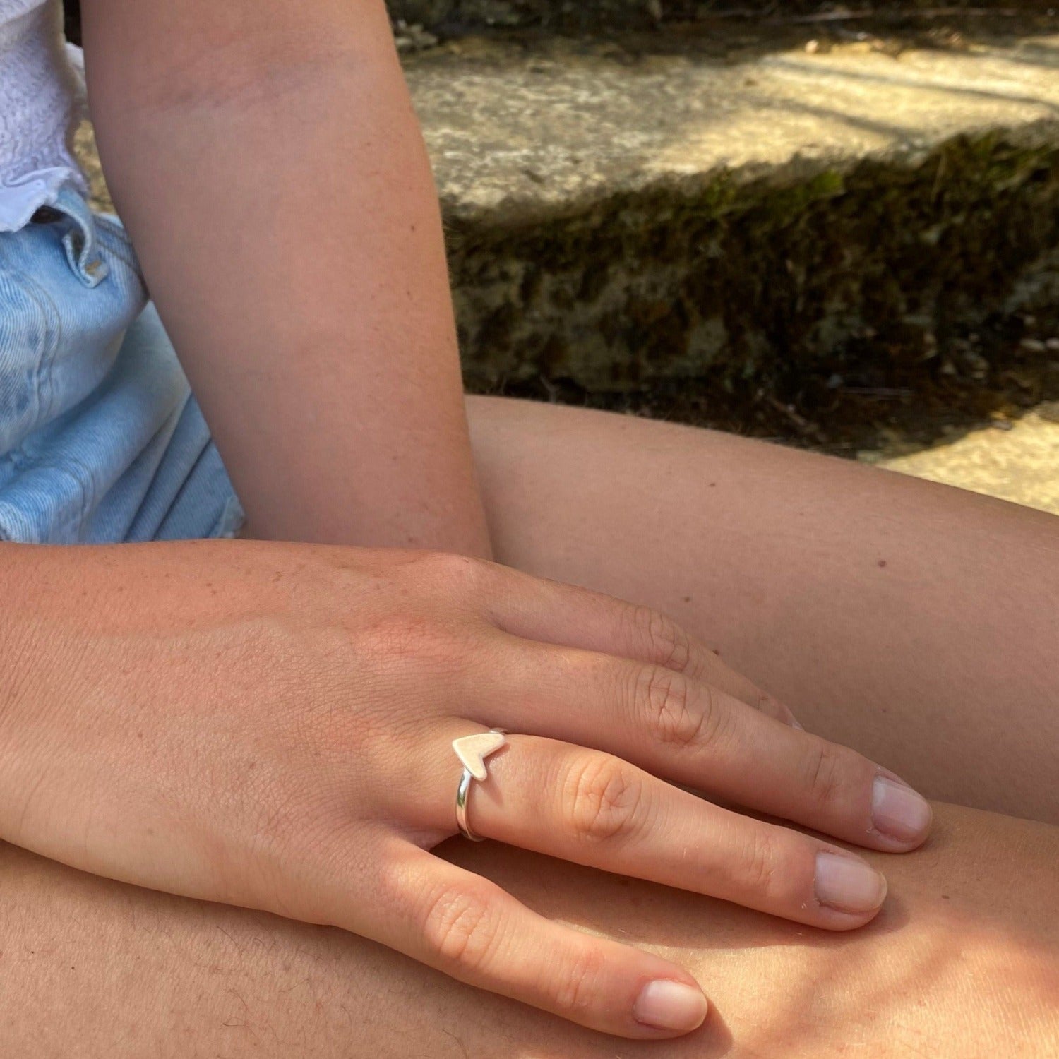 Silver adjustable banded ring with a heart as the central detail, worn on a woman's finger.