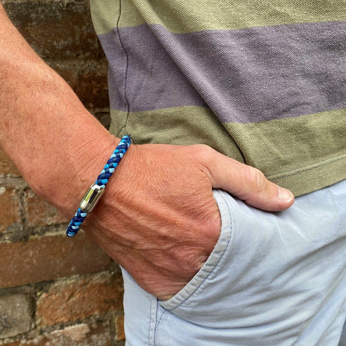 A blue plaited leather bracelet, finished with a stainless steel magnetic clasp and shown on a mans wrist.