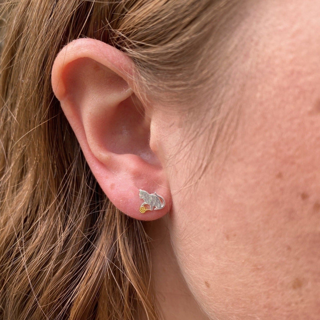 A sterling silver cat stud earring, playing with an 18ct gold plated ball of wool. Shown in a ladies ear.