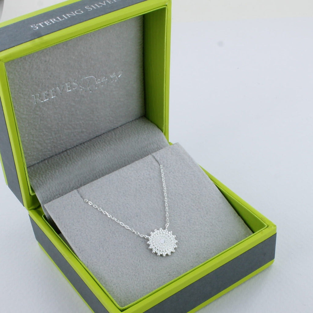 A Sterling Silver necklace in the shape of a catherine wheel necklace and hung centrally on a fine silver chain. Shown in a Reeves & Reeves grey and green branded gift box.