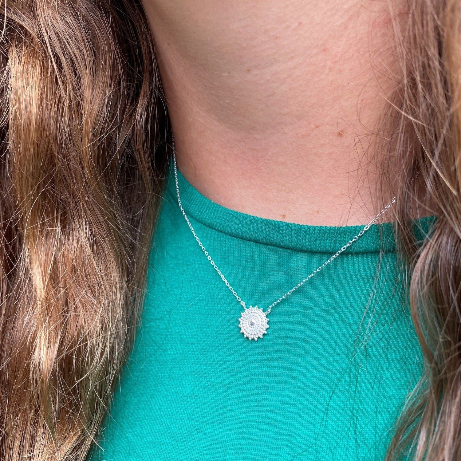 A Sterling Silver necklace in the shape of a catherine wheel firework, hung centrally on a silver adjustable chain and worn on a models neck.