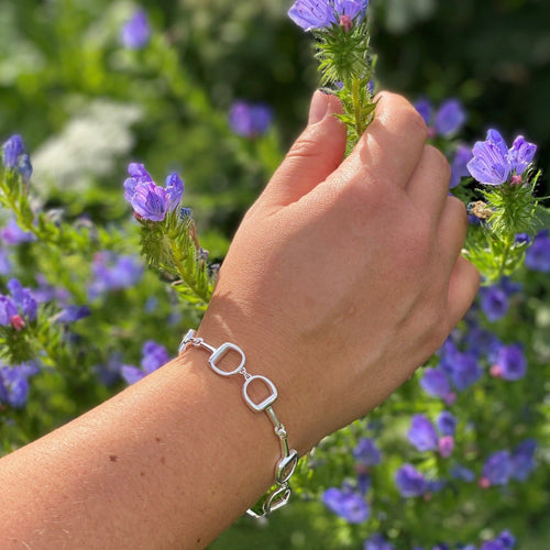 A chunky snaffle bracelet in sterling silver, with snaffles that wrap around the wrist. Shown on a ladies wrist holding a flower.