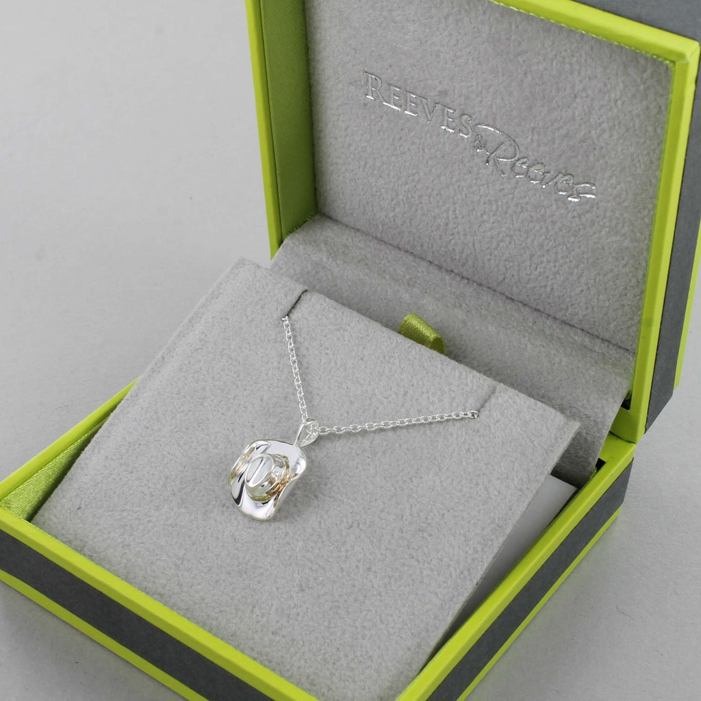 A silver cowboy hat pendant hanging on a silver chain and shown in a Reeves & Reeves grey and green gift box.