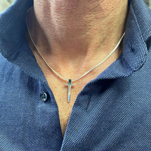 A sterling silver cross pendant, on a silver snake chain and worn on a male model.