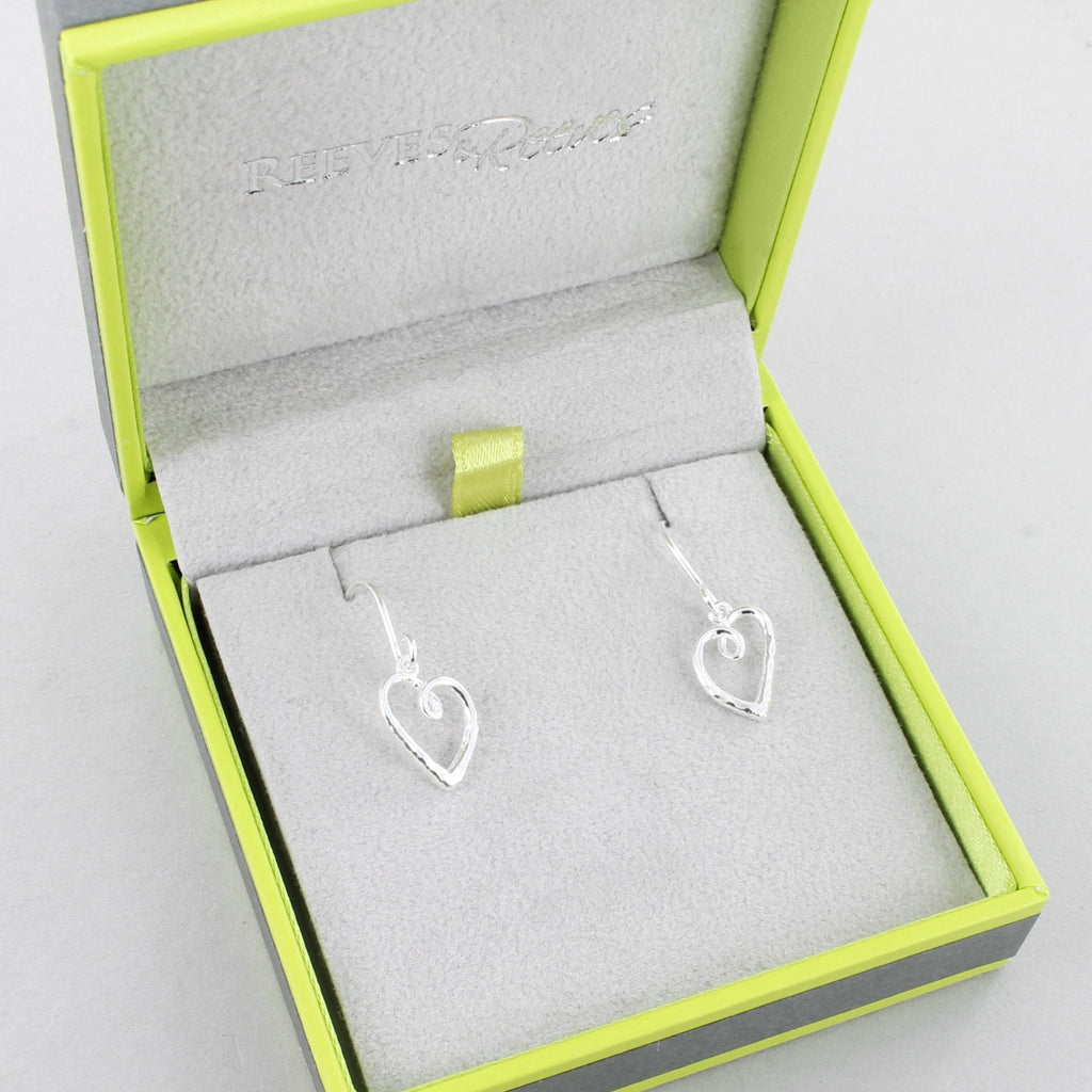A pair of sterling silver curly heart silhouette earrings with a textured finish, hanging on a silver hook and shown in a Reeves & Reeves gift box.