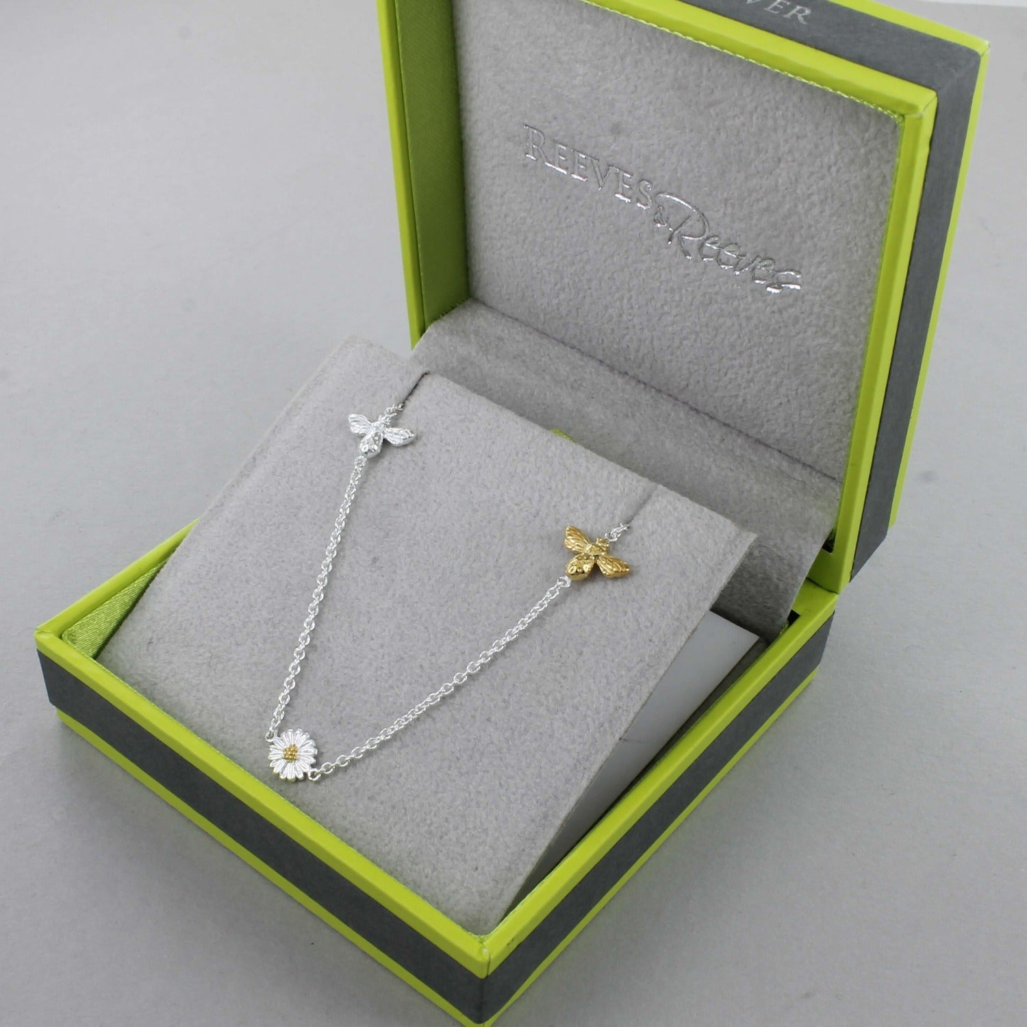 A Sterling Silver chain necklace with a silver bee, gold plated bee and a daisy spread evenly along the chain. Shown in a Reeves & Reeves grey and green gift box.
