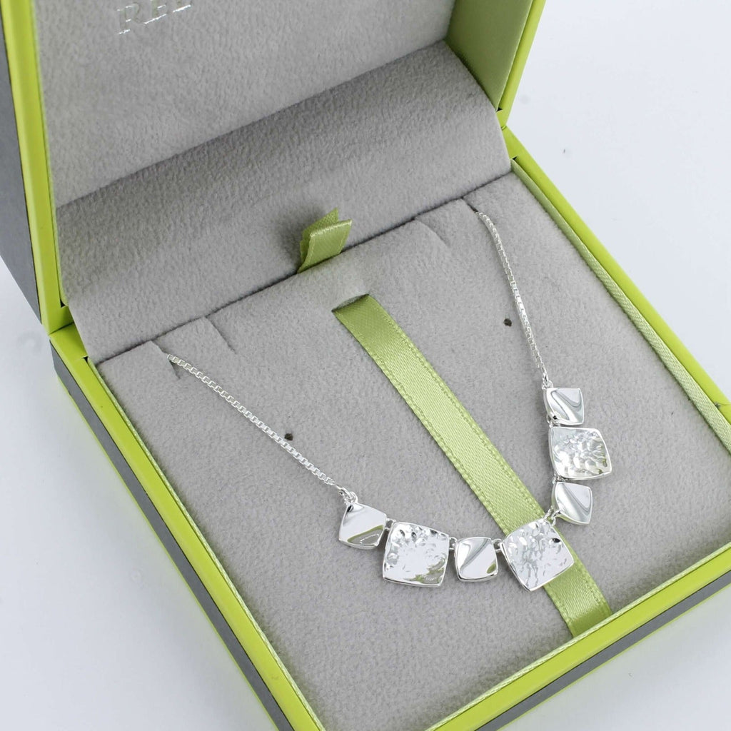A sterling silver necklace comprising of seven squares, the smaller in high shine and the larger in a hammered finish. Sitting centrally on a fine silver chain and shown in a Reeves & Reeves grey and green gift box.