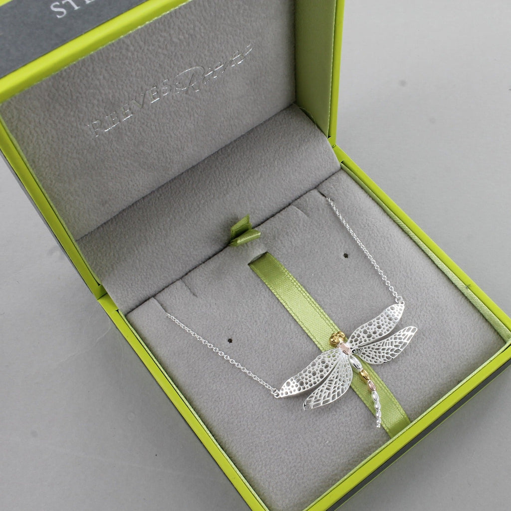 A Sterling Silver Dragonfly Necklace, with cut out wings and 18ct yellow and rose gold plate finish on its body. Hung on a silver chain and shown in a Reeves & Reeves grey and green branded box.