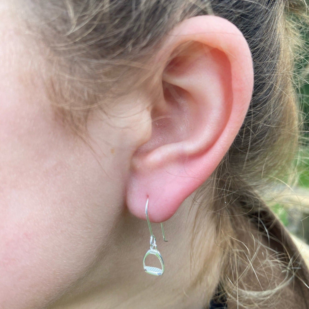 A sterling silver stirrup drop earring, hanging on a silver hook and shown in a ladies ear.