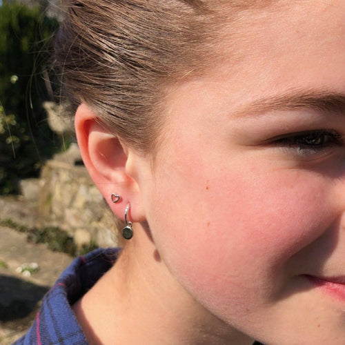 A sterling silver huggie style earring, with a high shine silver disc charm hanging from the bottom. Worn in a ladies ear.