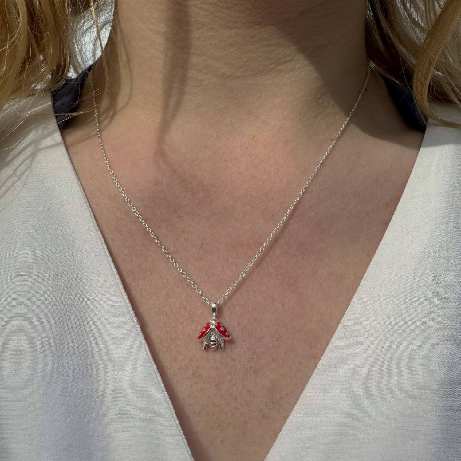 Sterling Silver Ladybird Necklace with red enamel detail on its wings. Hung on a silver adjustable chain and worn on a models neck.