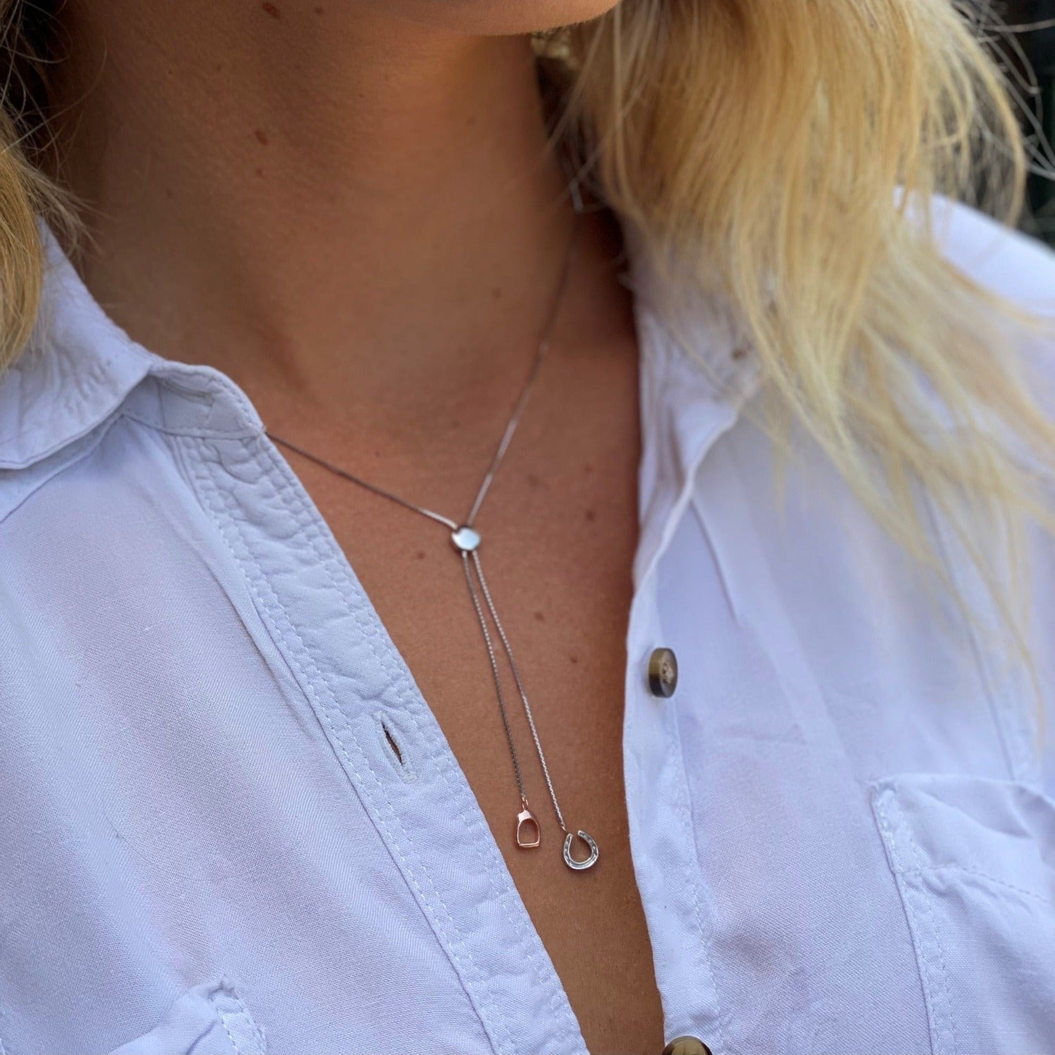 A falling stirrup and horseshoe necklace, shown on a models neck.