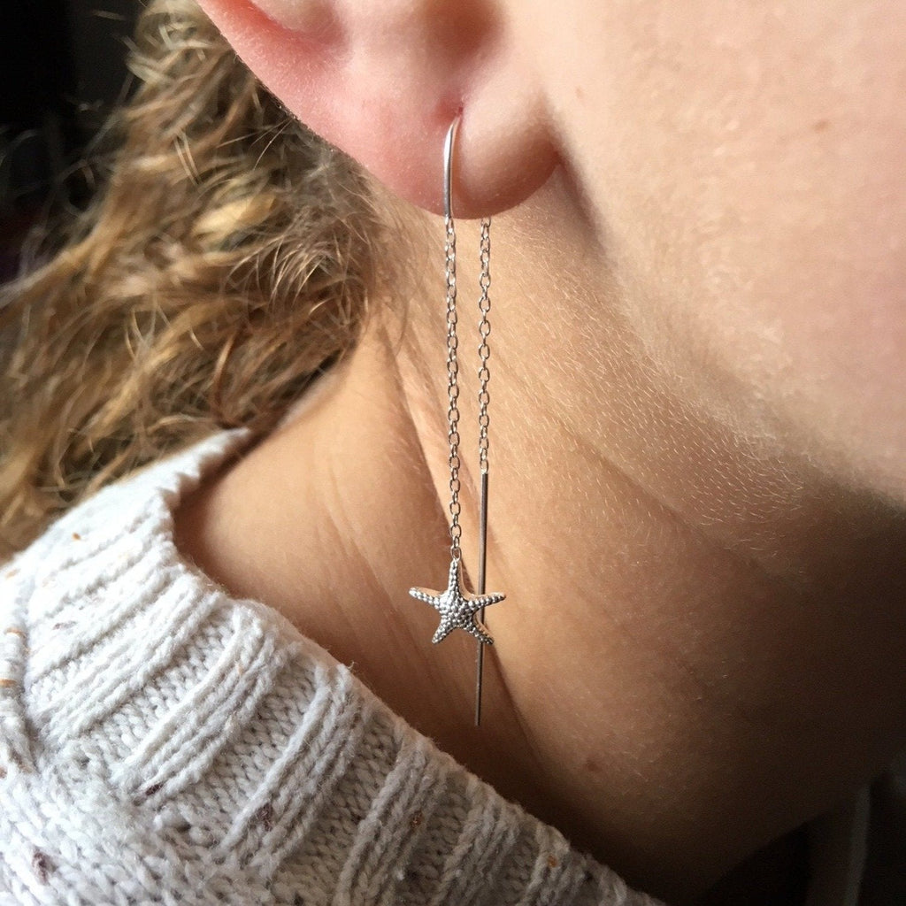 A sterling silver pull through style earring with a starfish hanging at each end, shown in a ladies ear.