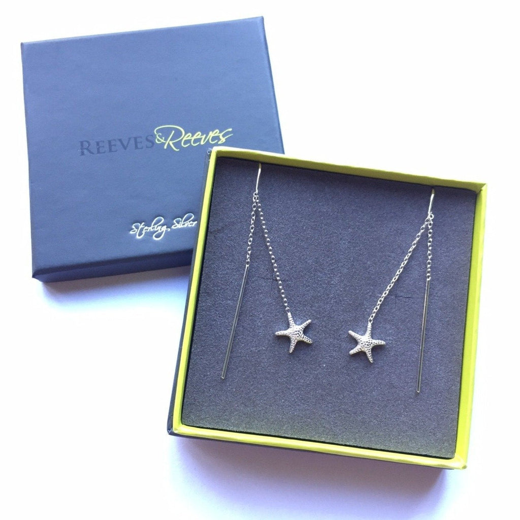 A pair of sterling silver pull through earrings, with a detailed starfish at each end of a fine chain. Shown in a Reeves & Reeves gift box.