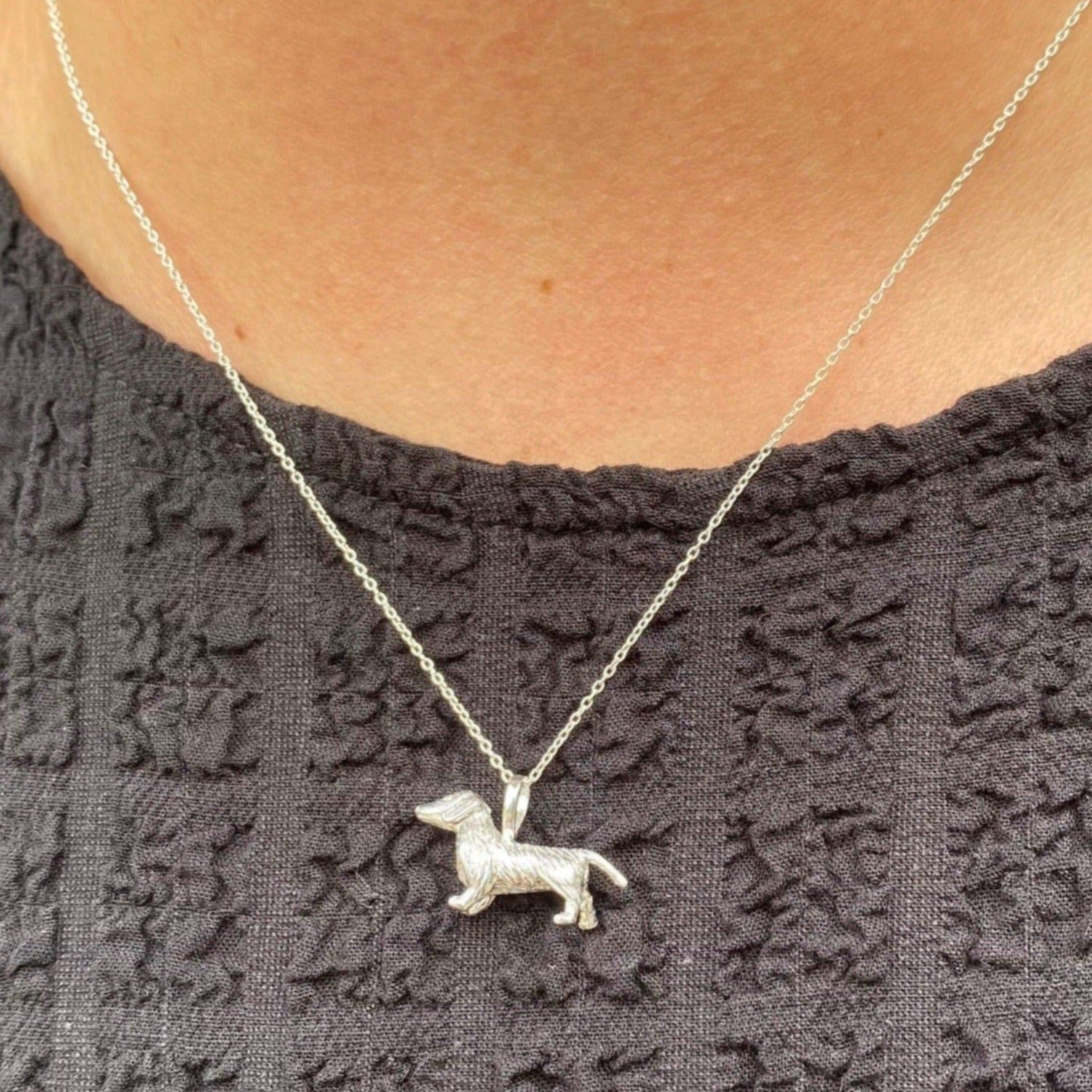Sterling Silver wire haired dachshund dog pendant, hanging on a silver chain and worn on a model wearing a black top.