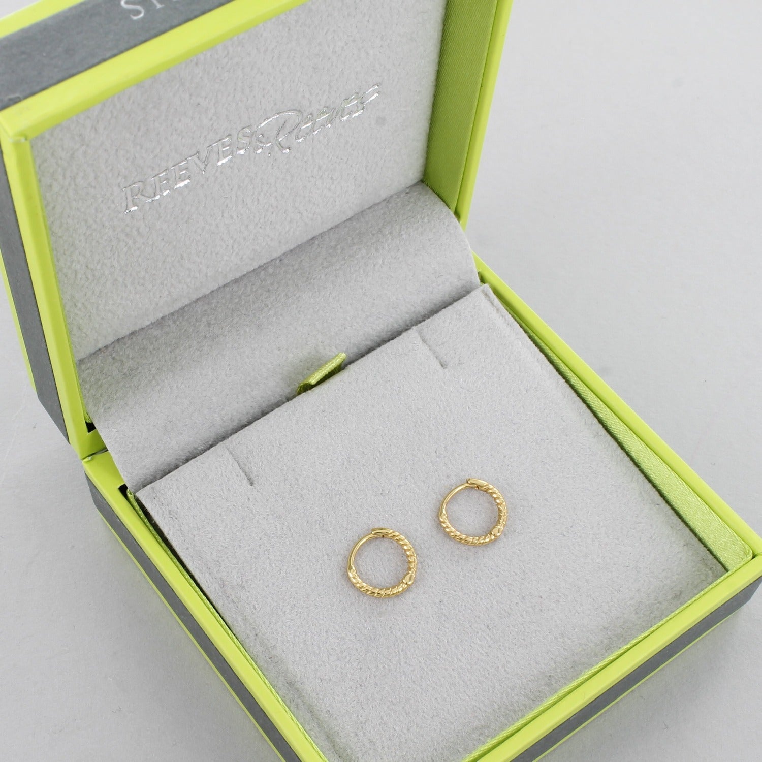 A pair of sterling silver and 18ct gold plated huggies that have a twisted rope effect to them, shown in a Reeves & Reeves gift box.