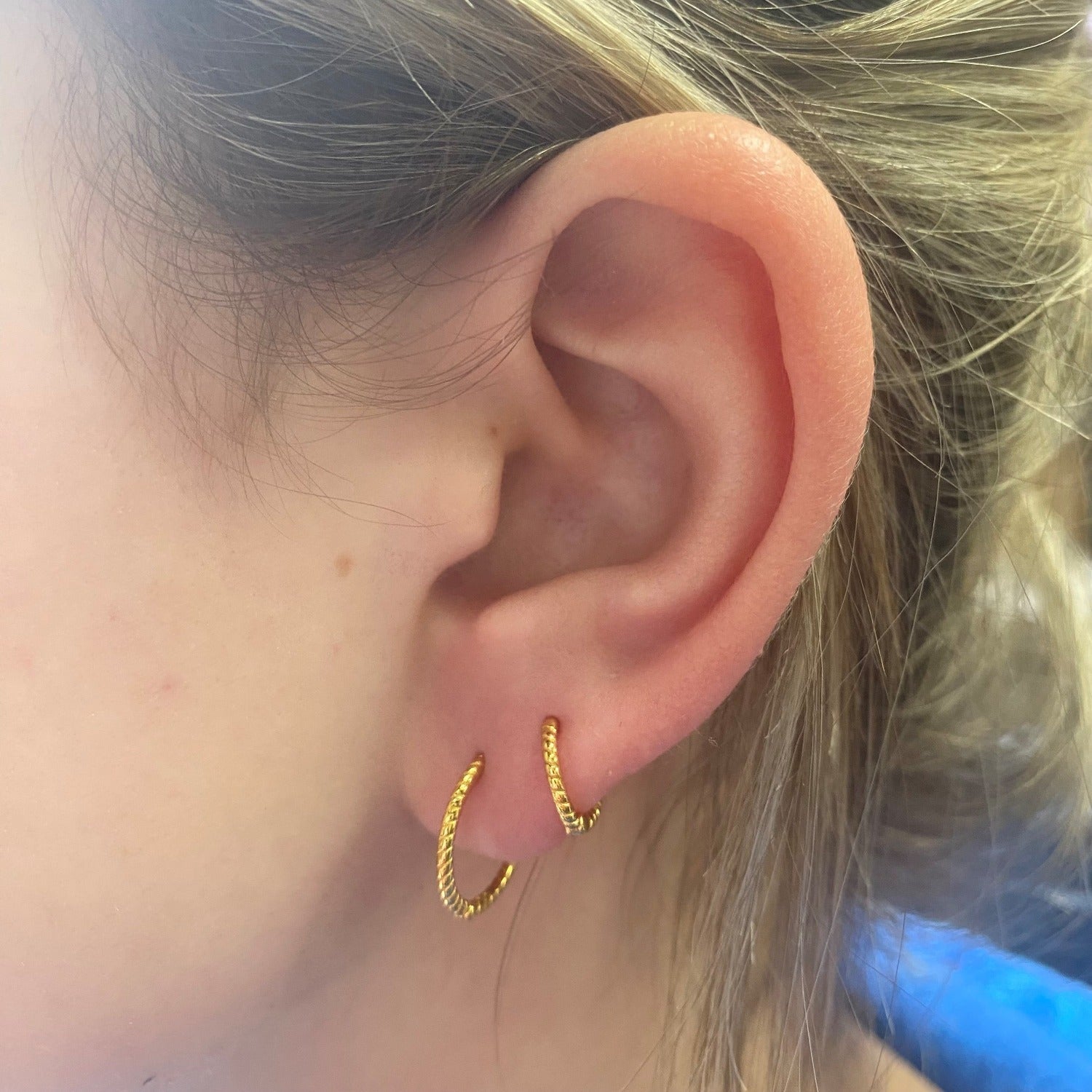 Two pairs of hoop earrings in two different sizes, shown in a ladies ear. Both hoops are sterling silver with 18ct gold plating and have a twisted rope effect to them.
