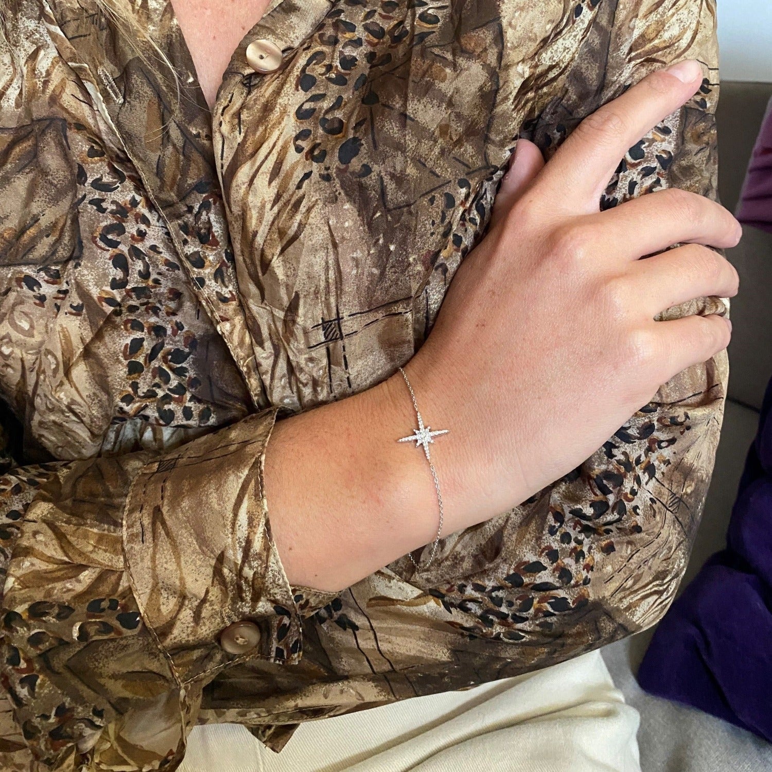 Silver fine chain bracelet worn on a women's wrist. The bracelet has an eight point star as the central feature.