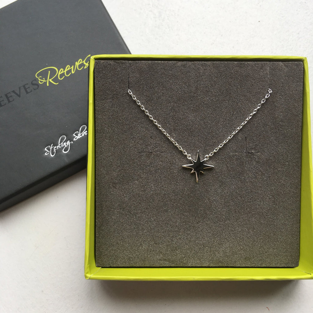 Sterling Silver eight point star necklace, sat centrally on a fine silver chain and shown in a Reeves & Reeves grey and green branded gift box.