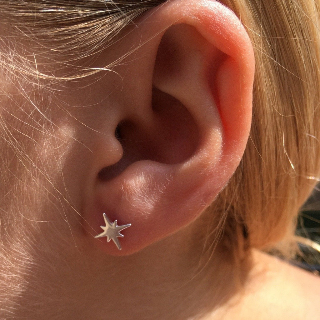 A sterling silver eight pointed star stud with a high shine finish, shown in a ladies ear.