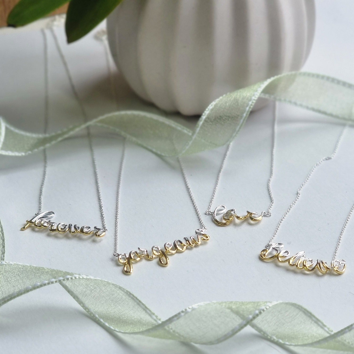 four script necklaces, with 'forever', 'gorgeous', 'love' and 'believe', in half silver and half 18ct gold plate, hung on silver chains.