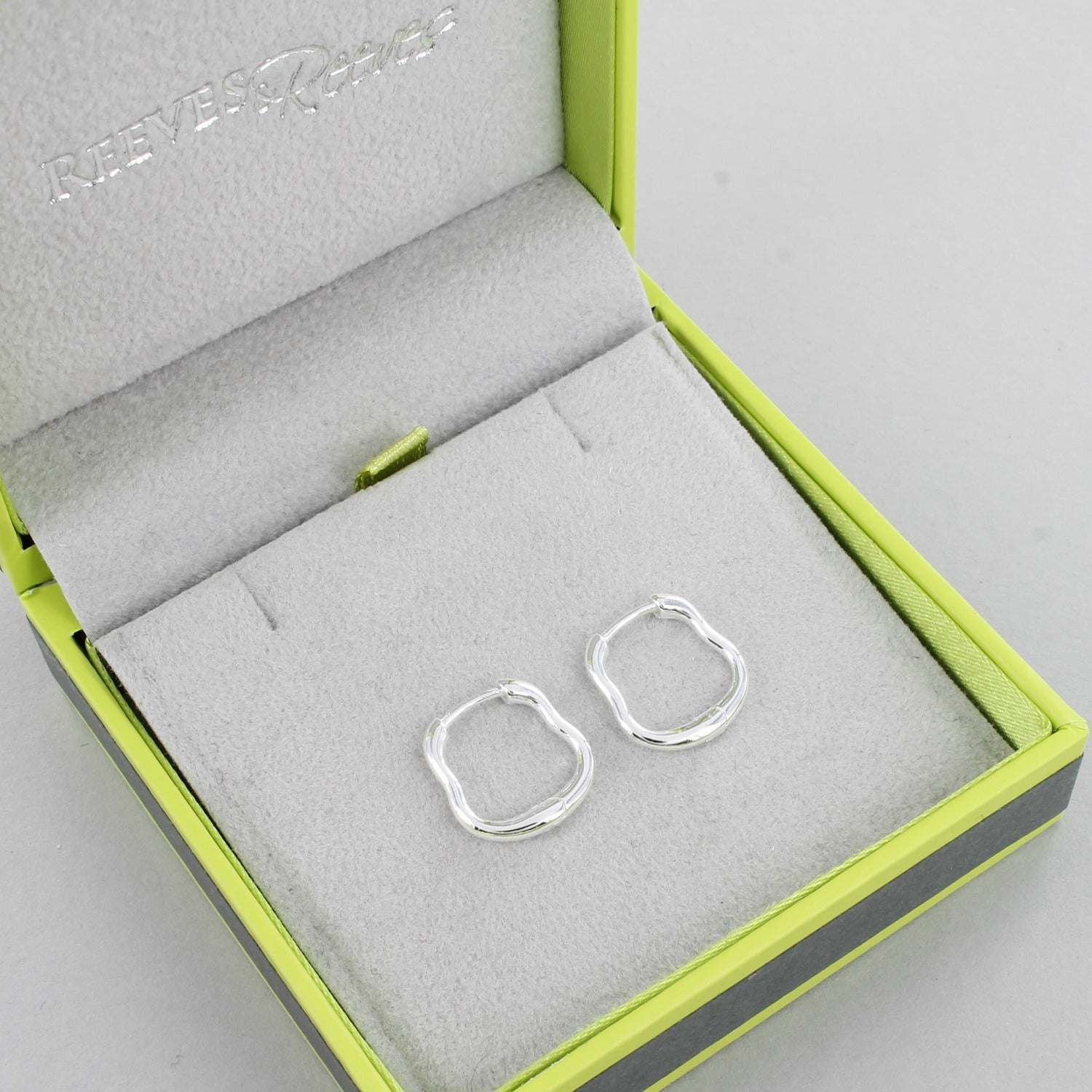 A pair of sterling silver hoop earrings with a wavy edge and shown in a Reeves & Reeves gift box.