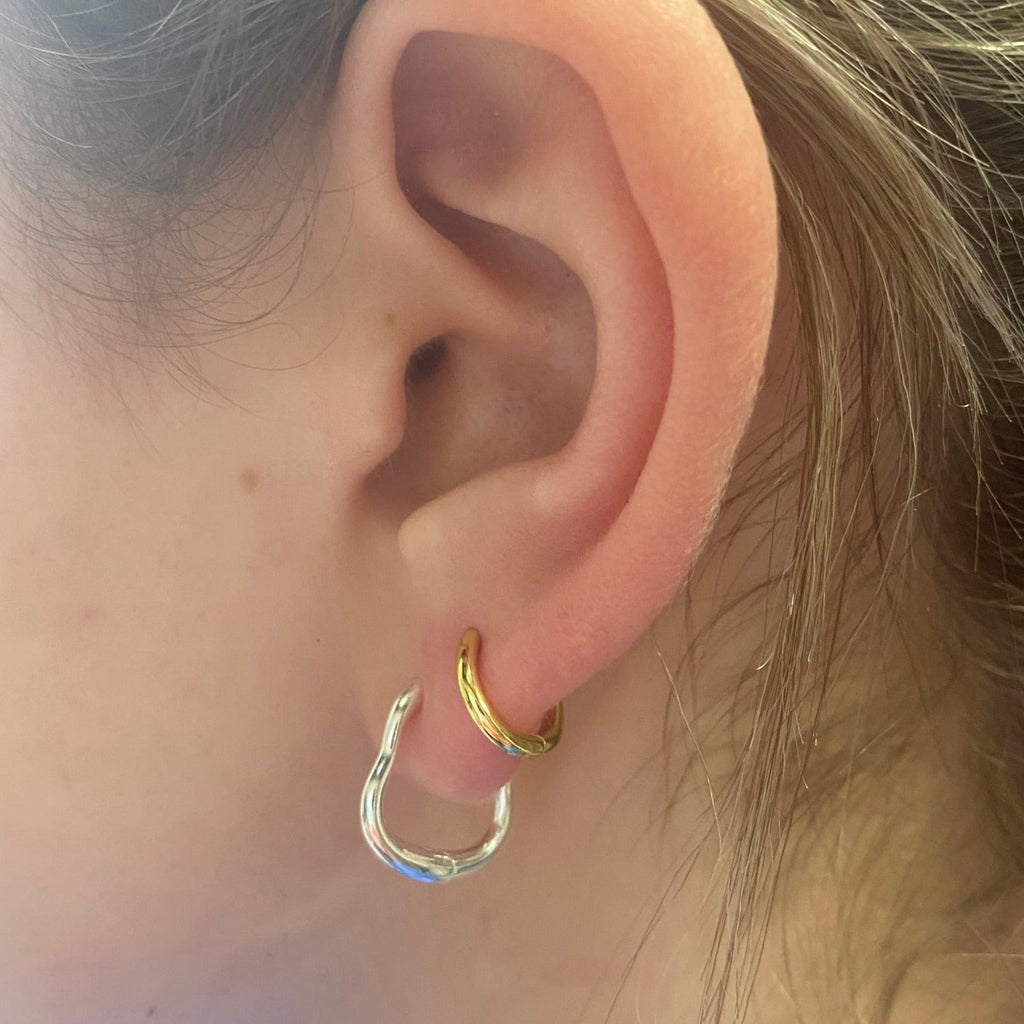 A sterling silver hoop earring, with a wavy edge, shown in a ladies ear with a smaller gold plated hoop.