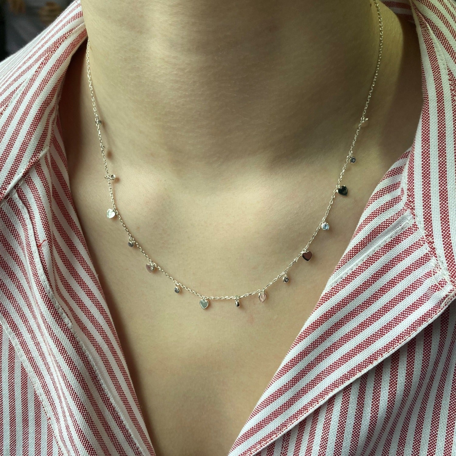 A sterling silver chain with small heart charms set evenly along the chain, interspersed with blue gem stones. Worn on a ladies neck.