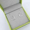 A pair of sterling silver heart shaped huggies, shown in a Reeves & Reeves gift box.