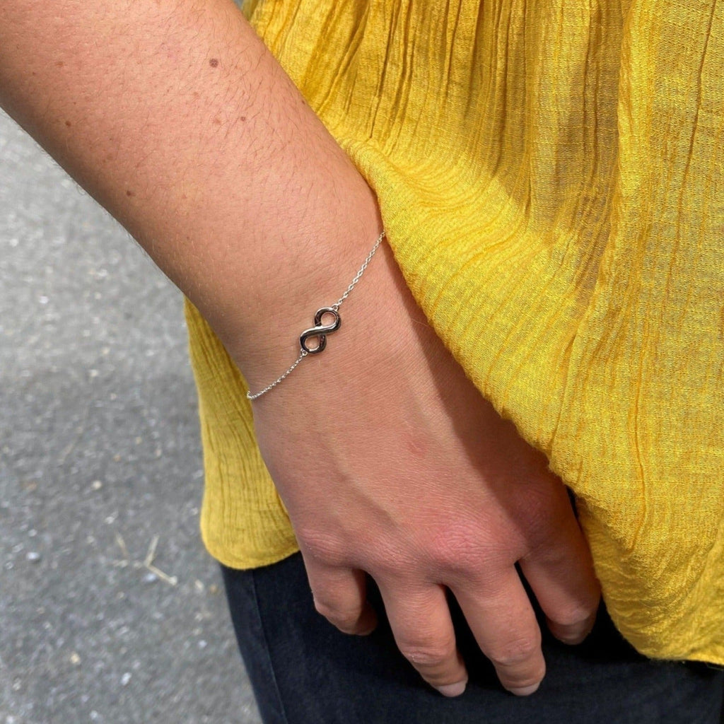 A chain style bracelet with an infinity symbol at the centre, worn on a women's wrist.
