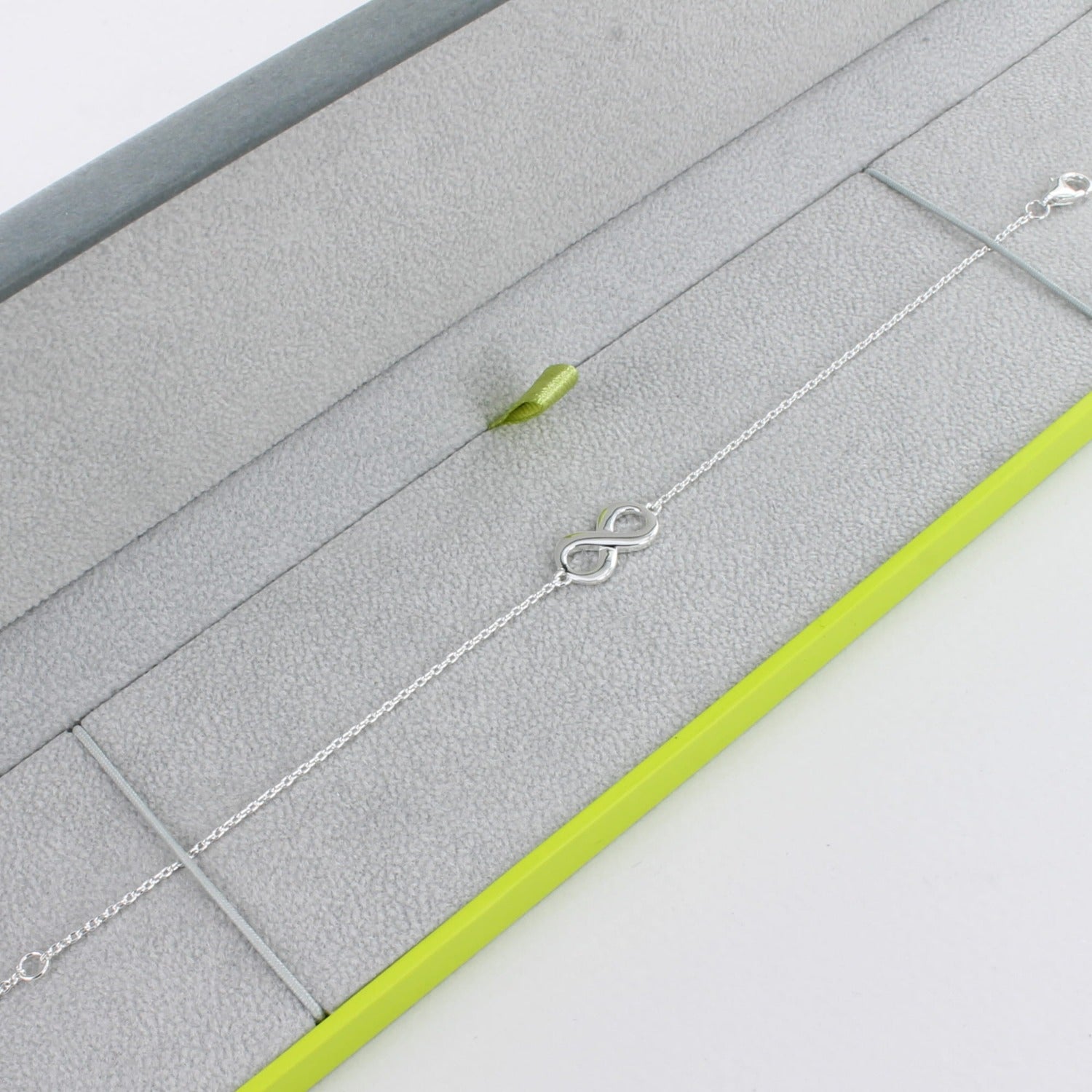 Silver chain bracelet with an infinity symbol at the centre and shown in a grey and green Reeves & Reeves branded box.